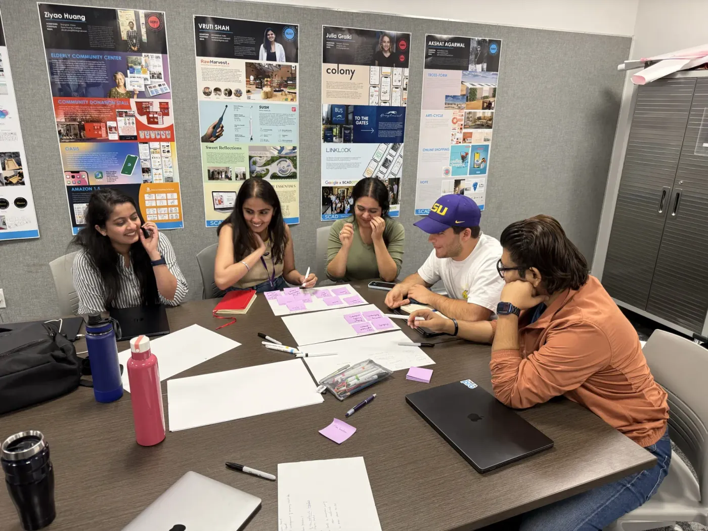 Five designers around a table during a playtest, debating sticky-note tasks and laughing