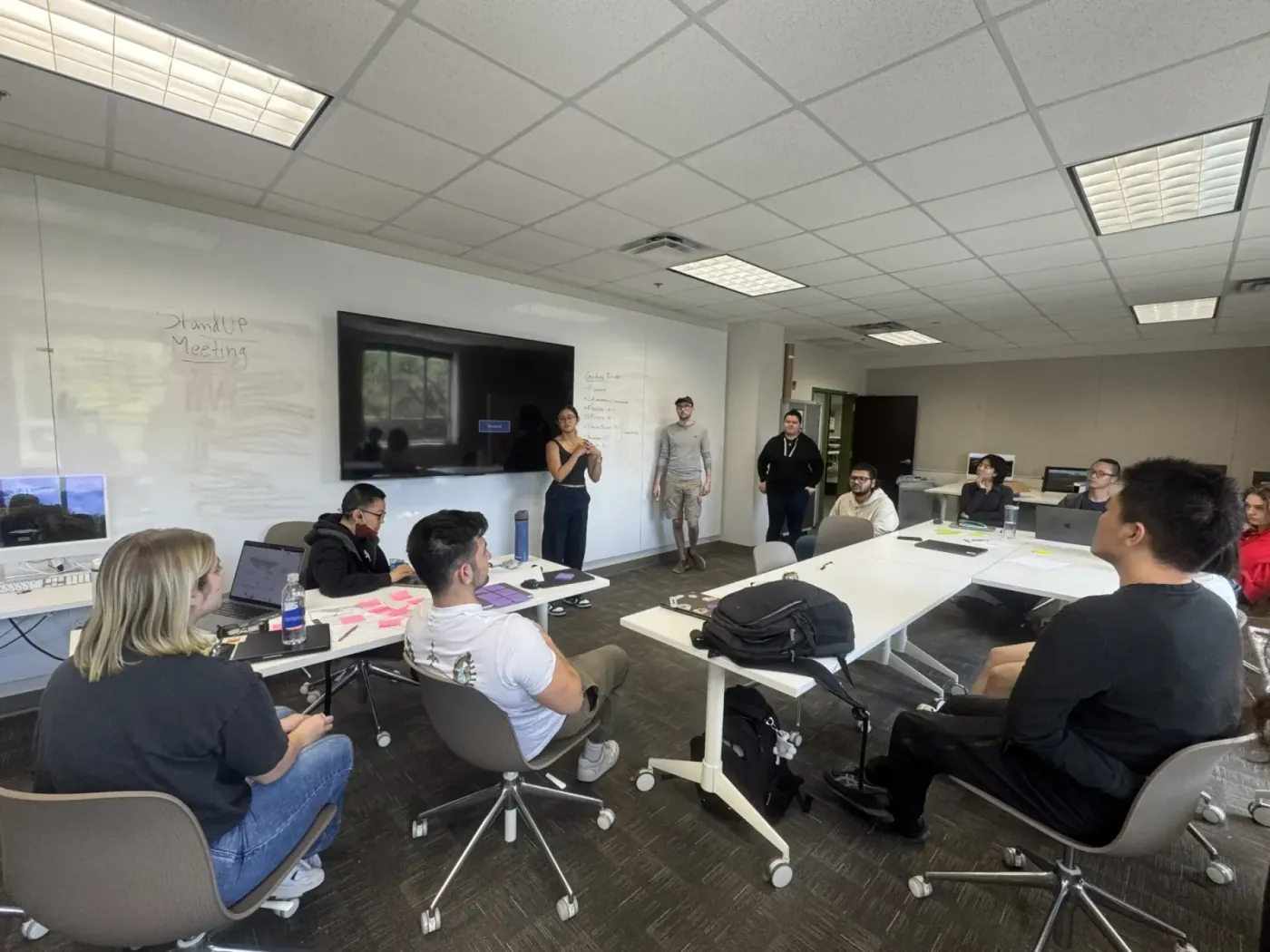 The team at a morning stand-up, standing and seated around tables